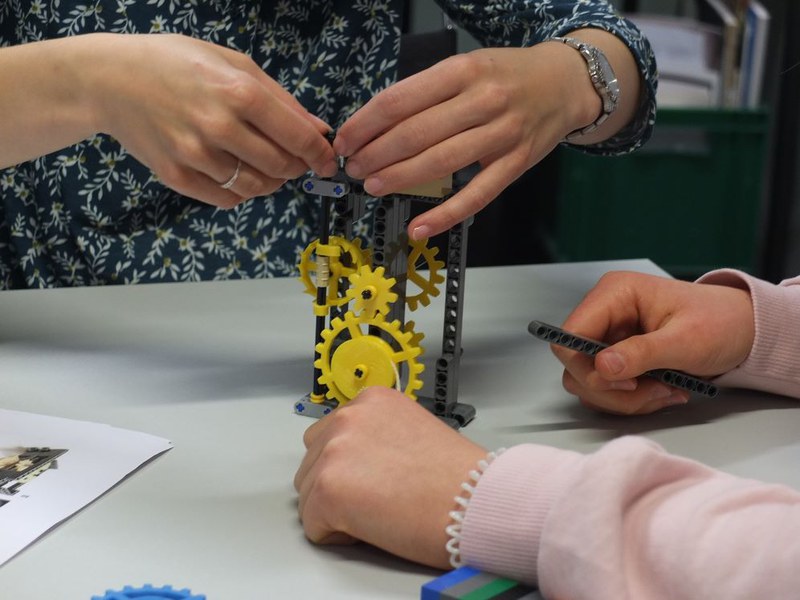 4 Hände arbeiten an einer Lego-Uhr