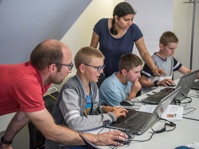 2 Erwachsene erklären 3 Kindern etwas auf den Laptops